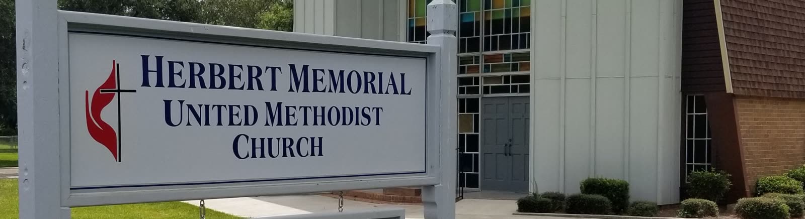 Church sign reading Herbert Memorial United Methodist Church, with the Cross and Flame, and the building behind it
